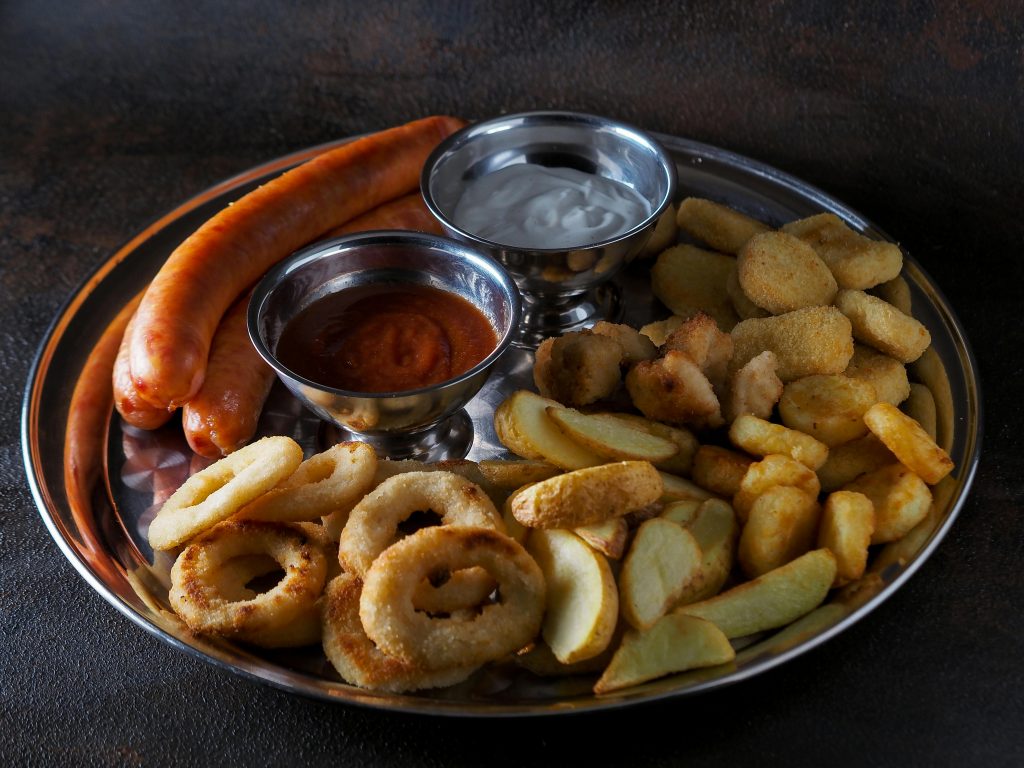 Delicious platter of sausages, fries, and dips served on a stainless steel plate.