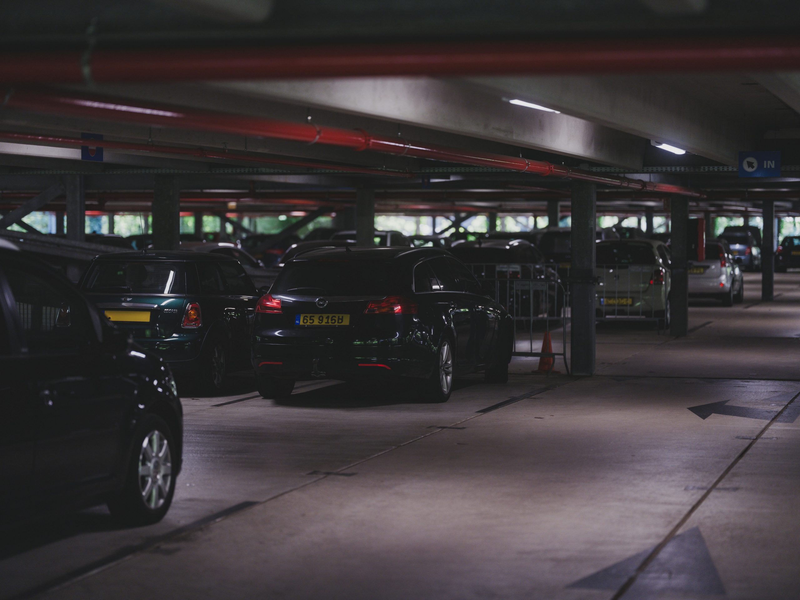 A dimly lit underground parking garage filled with parked cars and visible entrance signs.