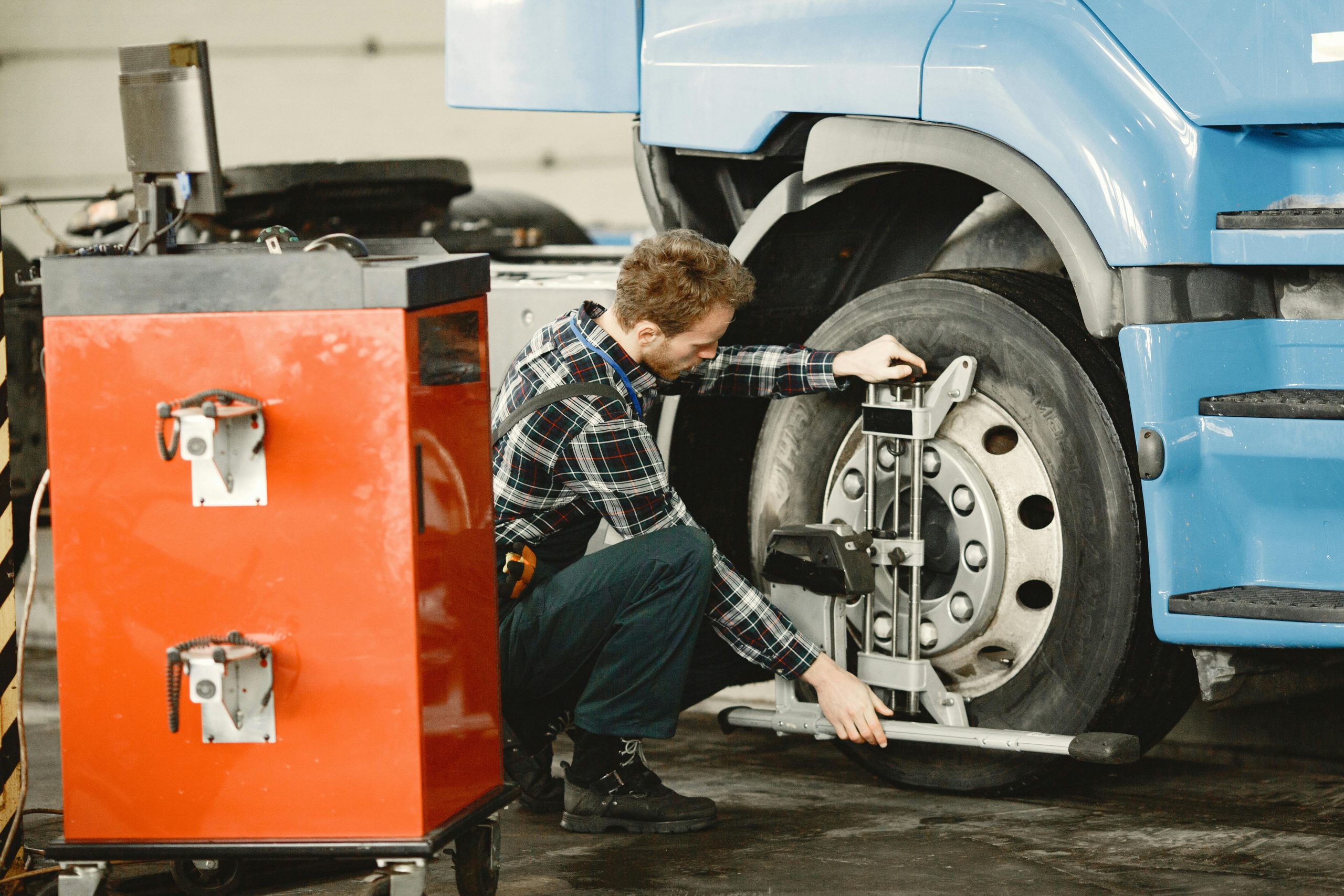 Mechanic performing tire alignment on a truck in an indoor workshop setting.