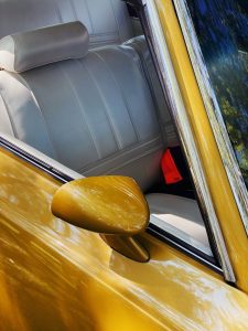 Close-up of a classic golden car with a sleek side mirror reflecting sunlight.