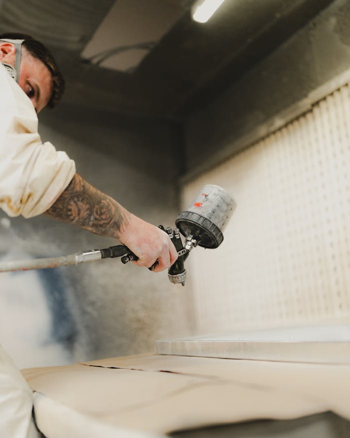 A man skillfully applies paint using a spray gun in an industrial environment.